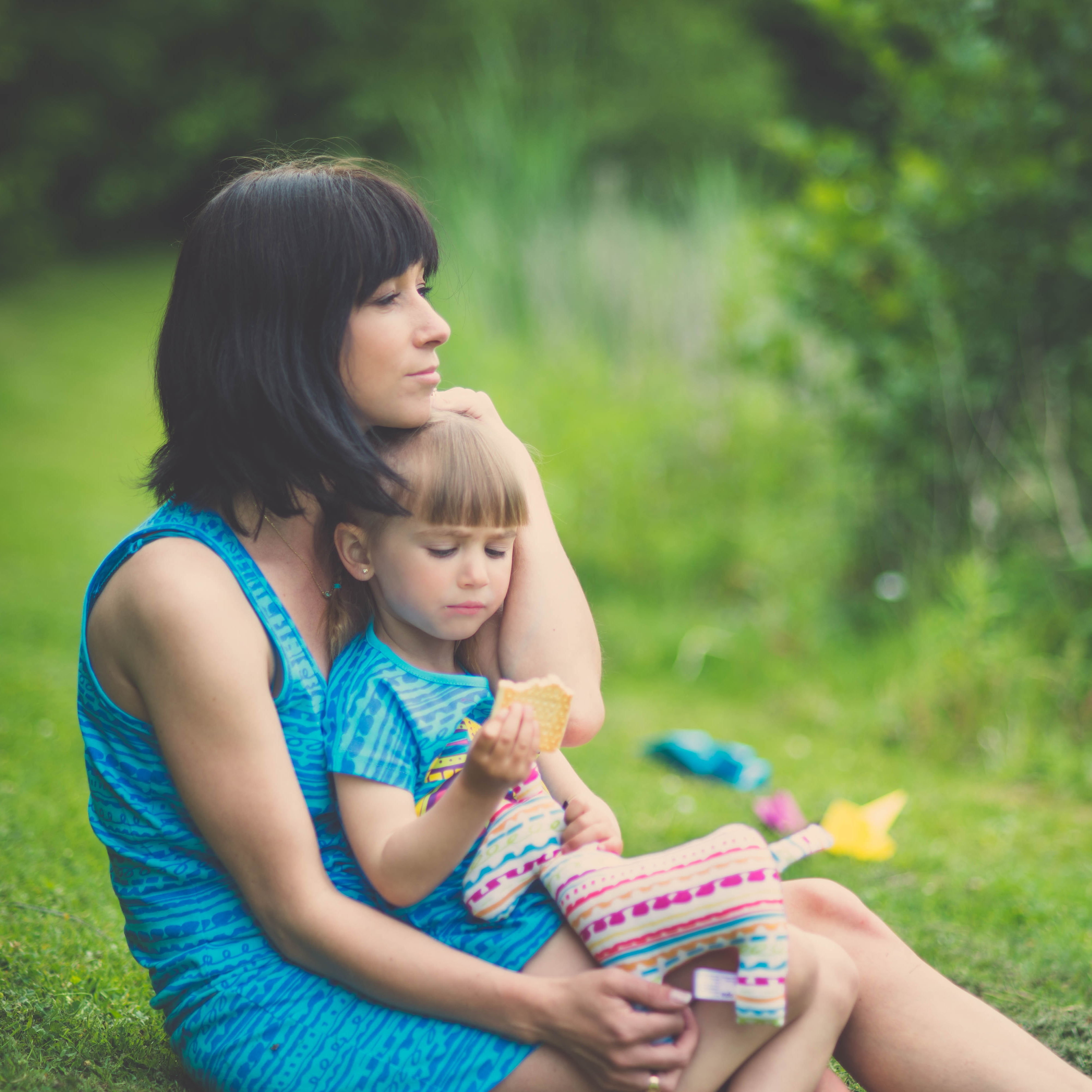 Mama trzymająca córkę na kolanach, siedząca na łące. Śmiejące się dziecko siedzące na kocu na trawie. Tata trzymający córkę na rękach.|Tata rozmawiający z synem.|Mama trzymająca córkę na kolanach na łące.|Monika Perdjon