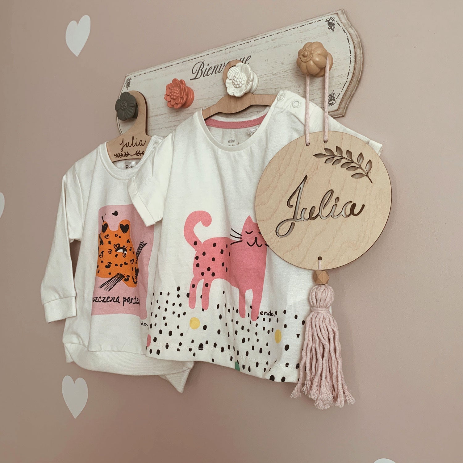 Dziecięce ubranka wiszące na drewniany wieszaczku na ścianie.|Dwie śpiące dziewczynki w różowych pajacykach.|Niemowlę ubrane na różowo leżące w pościeli.|Uśmiechnięte niemowlę leżące na kocyku w pieski.|Roześmiane niemowlę leżące na białym prześcieradl...