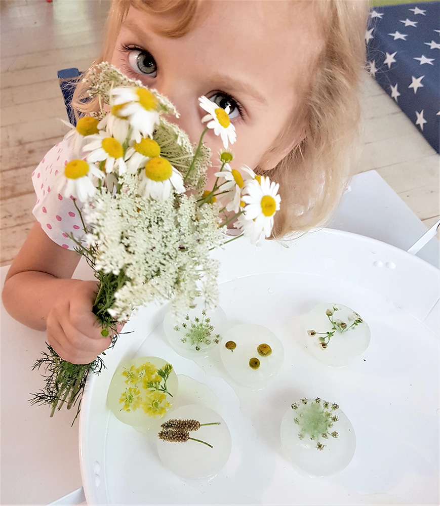 Dziewczynka zasłaniająca buzię bukietem biało żółtych kwiatków.