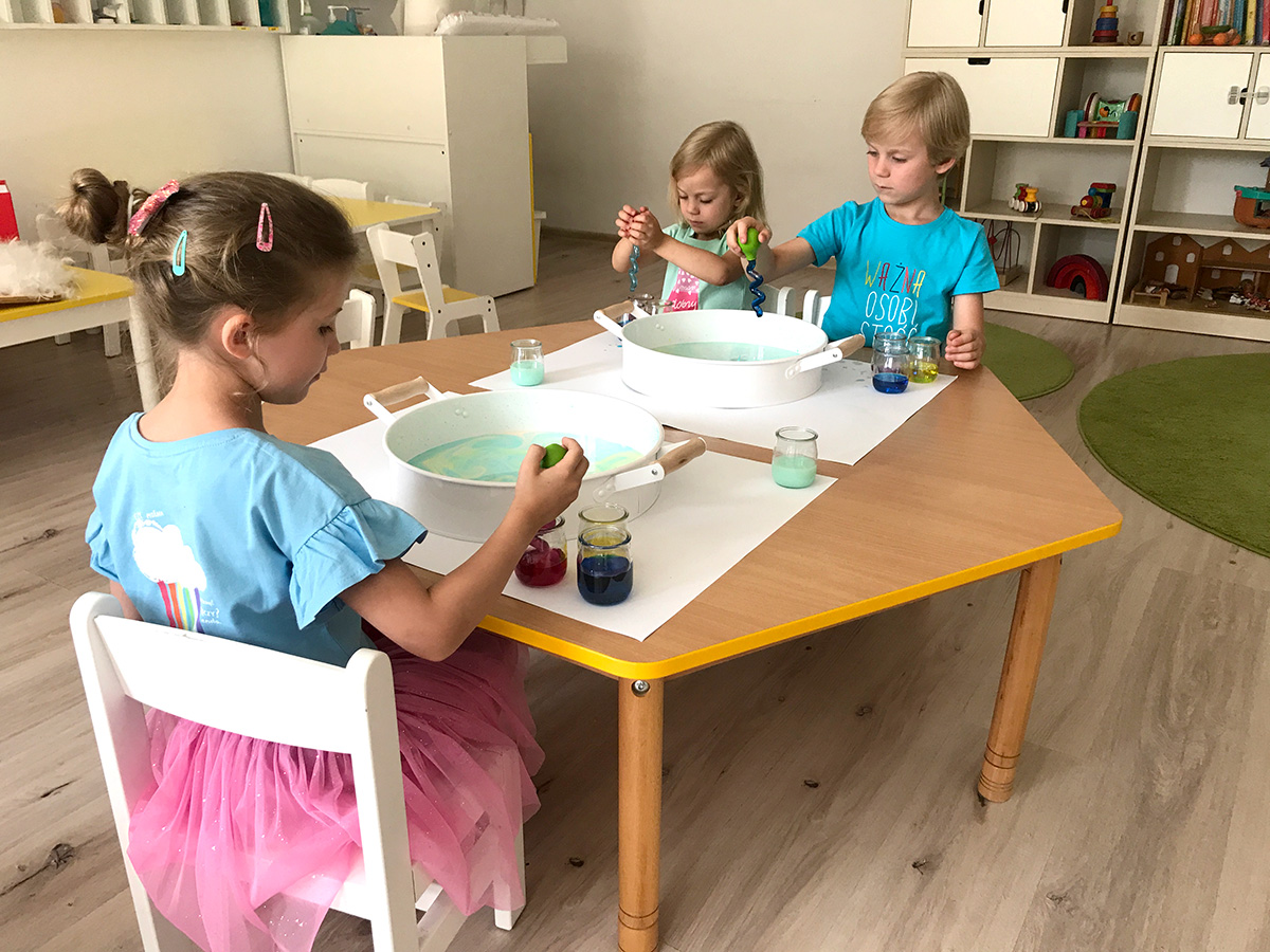 Dzieci wlewające kolorowe barwniki do naczynia z mlekiem