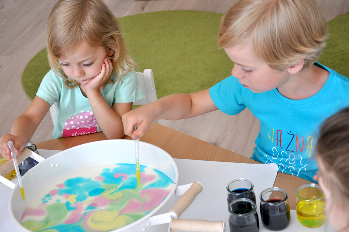 Dziewczynka z chłopcem malujący na mleku kolorowymi smugami