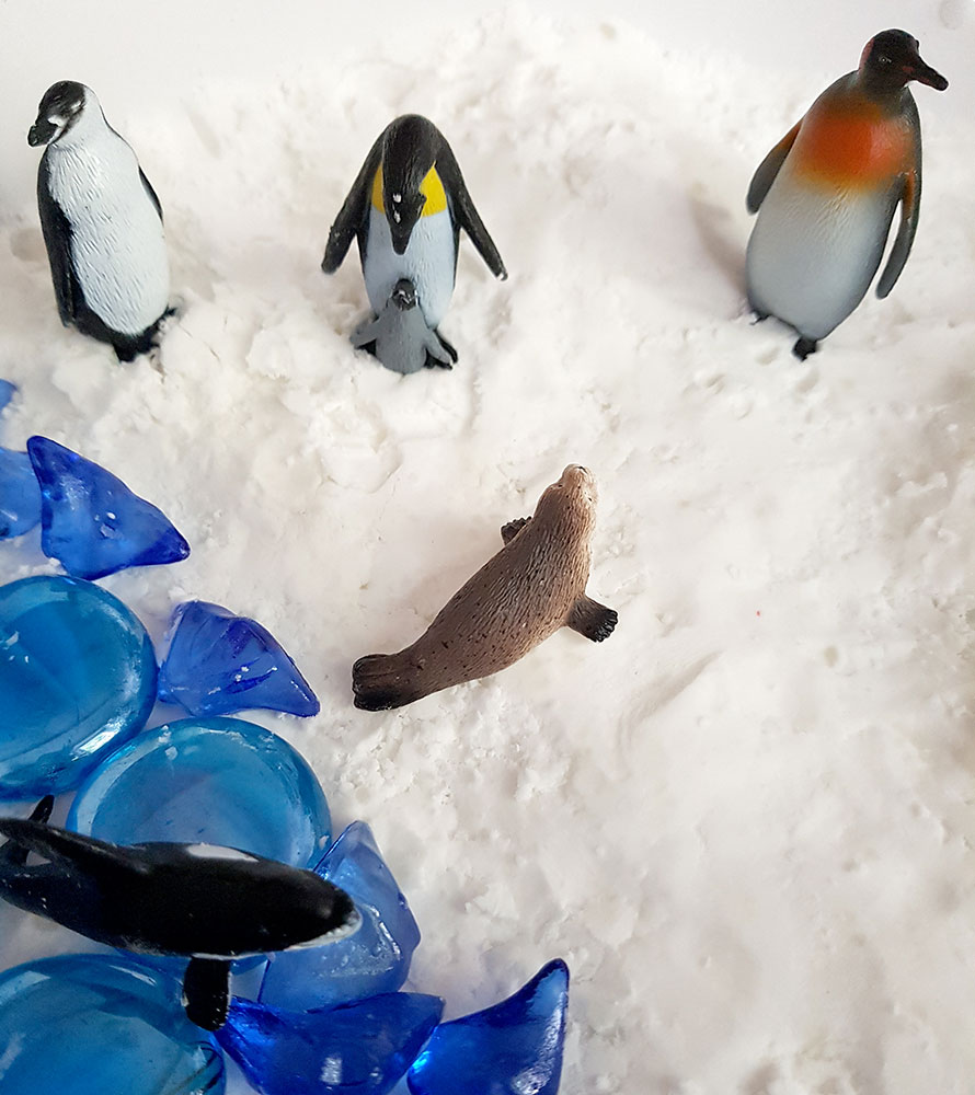 Arktyczne zwierzęta zabawki ułożone na sztucznym śniegu i niebieskich koralikach.
