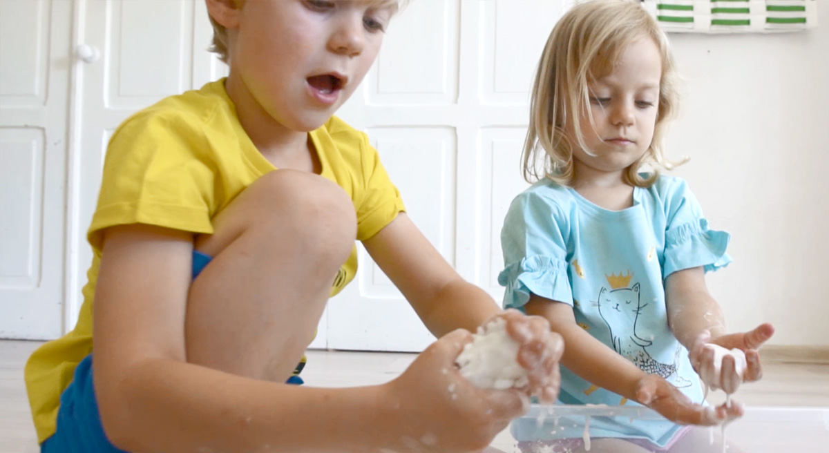Dzieci ugniatają mąkę z wodą w rączkach podczas zabawy.