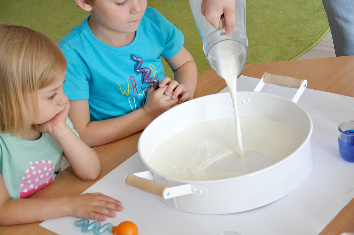 Dziewczynka z chłopcem przyglądający się wlewanemu mleku do miski