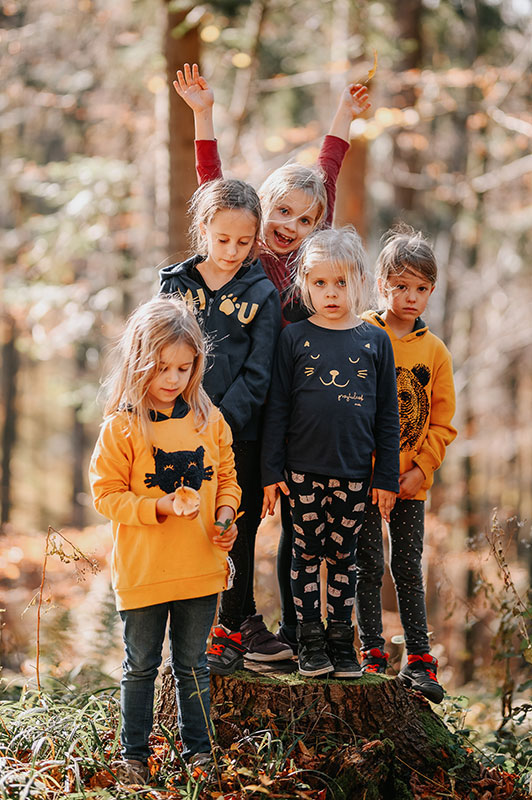 Dzieci stojące w kolorowych ubrankach na pniu w lesie.
