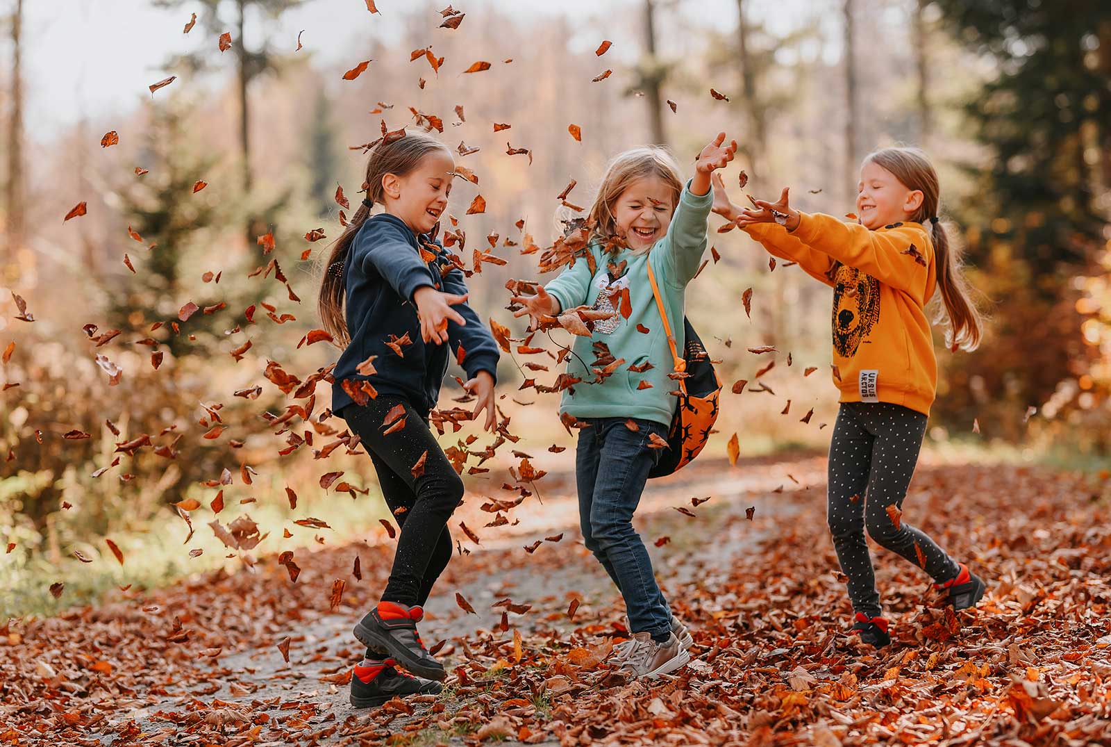 Trzy roześmiane dziewczynki obrzucają się jesiennymi liśćmi.