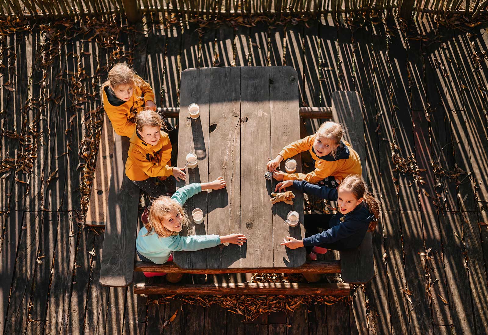 Grupka dzieci siedzi przy stole na dworze popijając gorącą czekoladę.