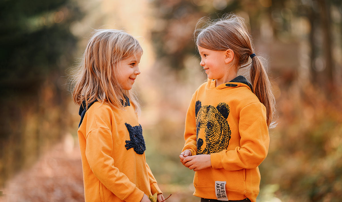 Dwie dziewczynki w żółtych bluzach na spacerze w lesie.