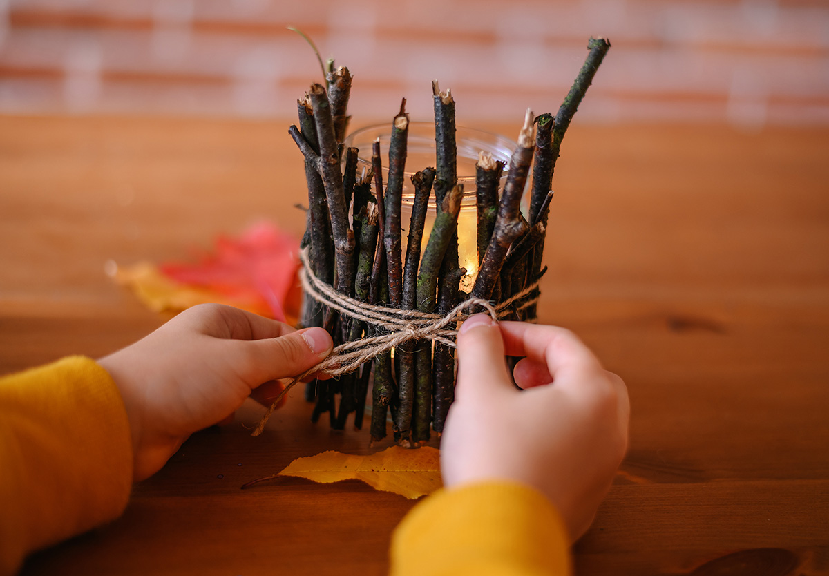 Jesienne zabawy dla dzieci - Dziecko wiąże kokardkę na świeczniku z patyków wykonanym własnoręcznie.