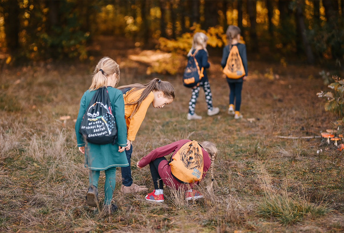 Jesienne zabawy dla dzieci - Grupa dziewczynek szuka patyczków podczas jesiennego spaceru w lesie.