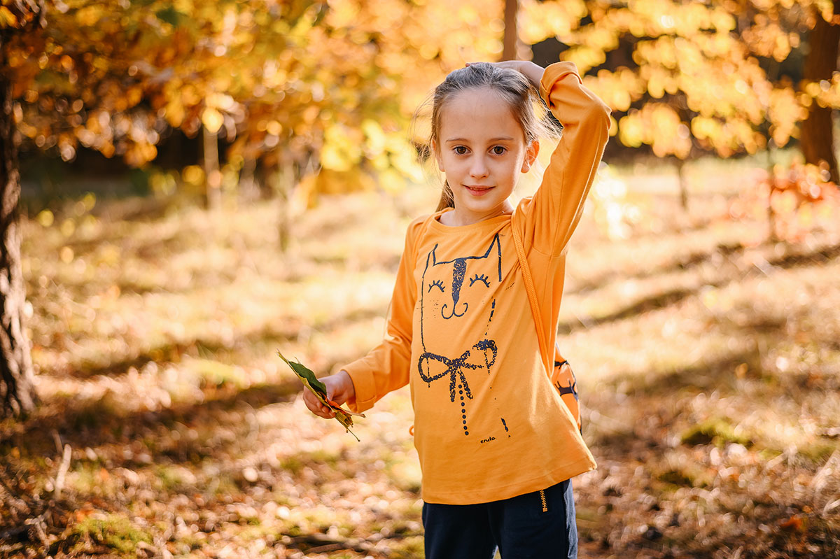 Jesienne zabawy dla dzieci - Mała dziewczynka w żółtej bluzce na tle jesiennego krajobrazu.