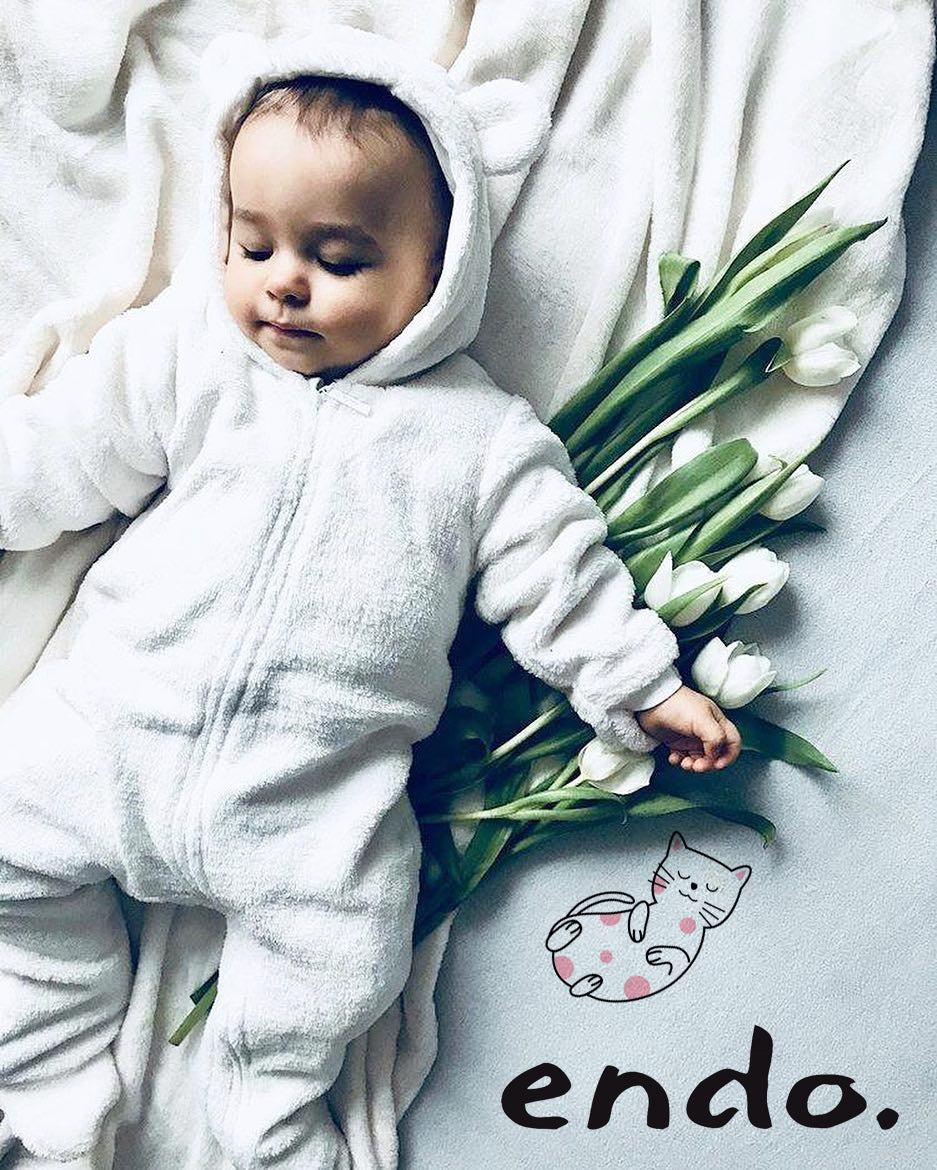 Niemowlę leżące w białym kombinezonie typu miś.